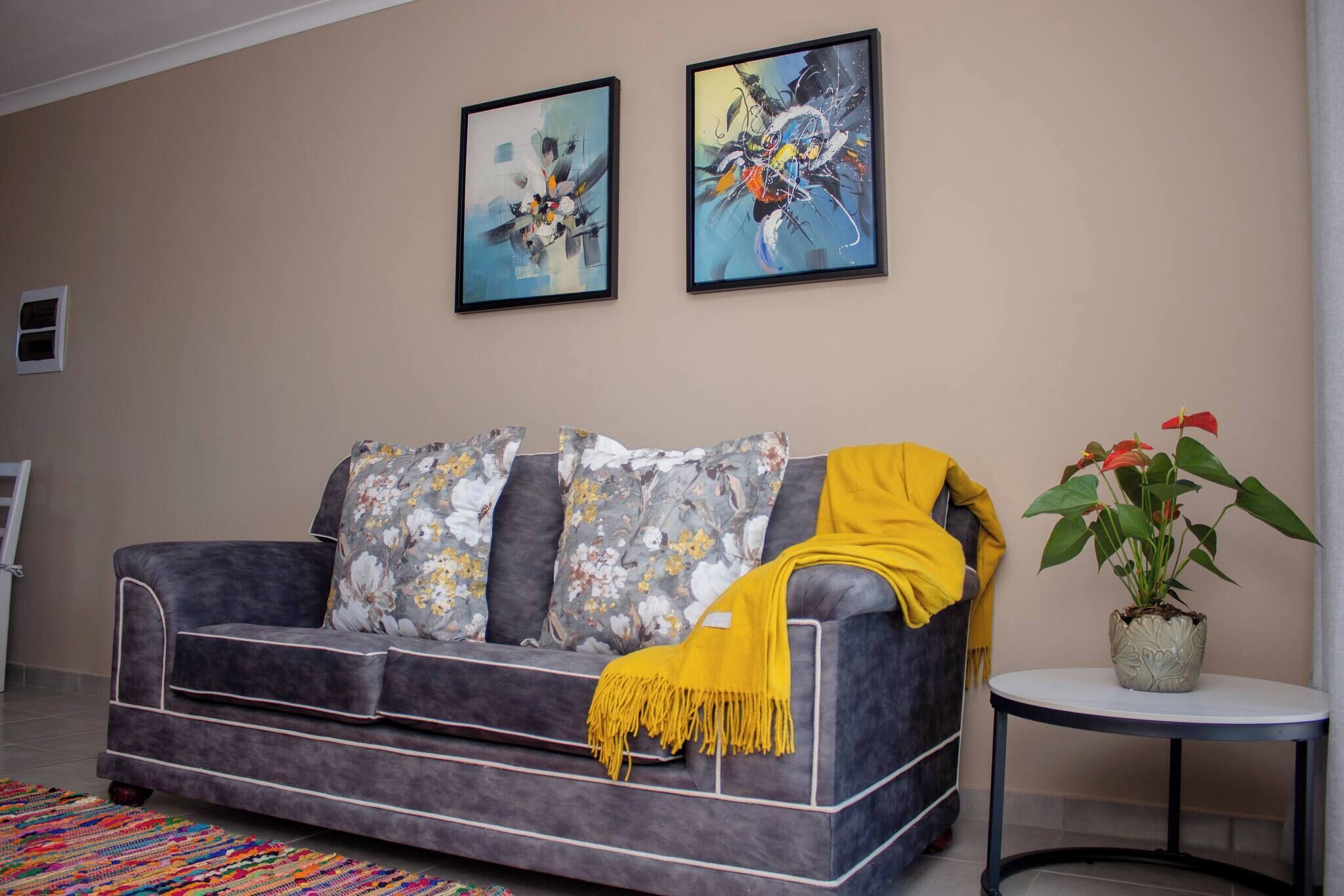 Ein Wohnzimmer mit grauem Sofa, floralen Kissen, einer gelben Decke und zwei gerahmten Kunstwerken an der Wand.