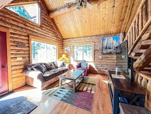 A log cabin interior with a sofa, coffee table, and a TV.