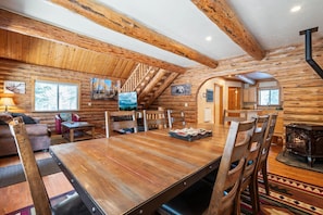 A log cabin interior with a dining area, a fireplace, and a staircase.
