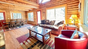 A log cabin interior with a dining area, a sofa, a red armchair, and a lamp. - North Star Cabin in Whitefish, near Glacier (Whitefish)