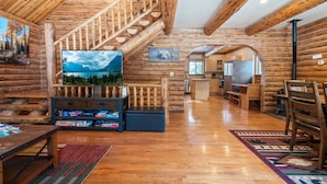 A log cabin interior with a wooden staircase, a television, a fireplace, and a kitchen area. - North Star Cabin in Whitefish, near Glacier (Whitefish)