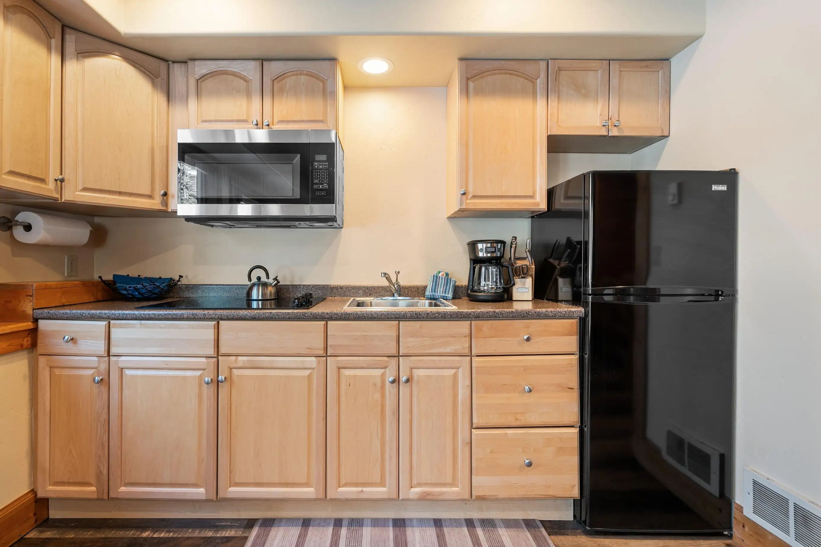 A kitchen with wooden cabinets, a stainless steel microwave, a black refrigerator, and a coffee maker.