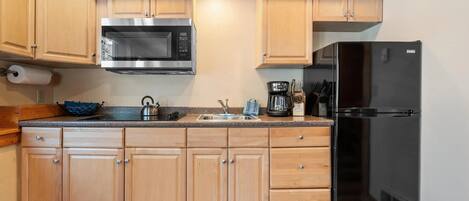 A kitchen with wooden cabinets, a stainless steel microwave, a black refrigerator, and a coffee maker.