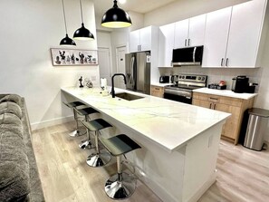 Eine moderne Küche mit weißen Schränken, einem Edelstahlkühlschrank, einer Mikrowelle, einer Kaffeemaschine und einer Bar mit Barhocker.