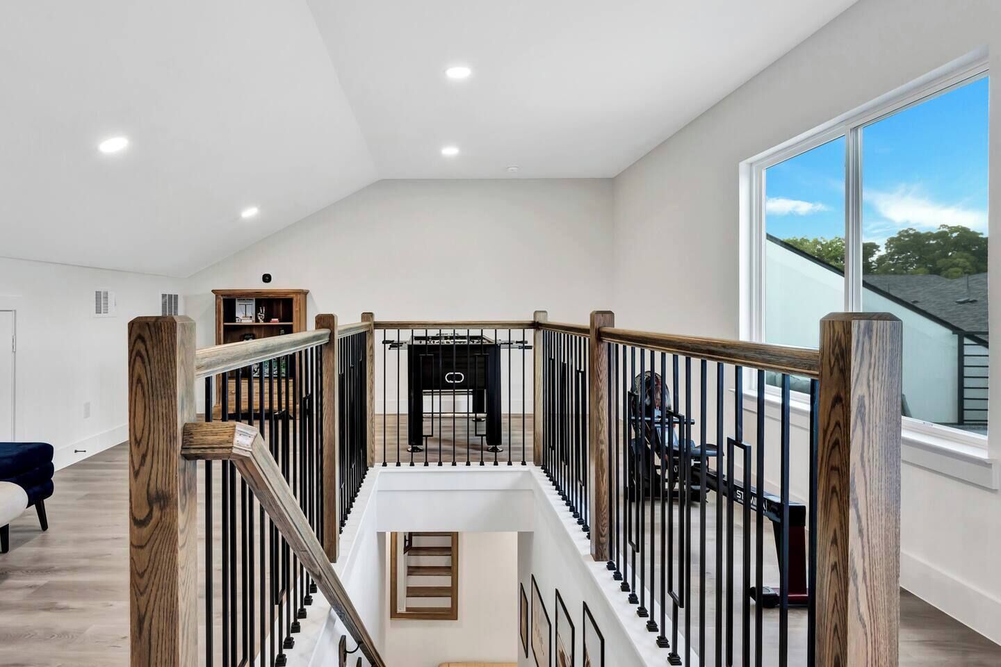 A spacious interior with a high ceiling, a staircase with wooden railings, and a large window offering a view of the outdoors.