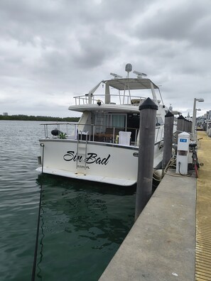 A white boat named 'Sin Bad' docked at a marina with a covered deck area and a small outdoor seating space.