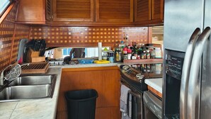A compact kitchen with wooden cabinets, a stainless steel sink, a refrigerator, and a small trash bin. - Enjoyable 4-bedroom boat with AC in vibrant Miami Beach (Miami Beach)