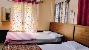 A hotel room with two beds, a ceiling fan, an air conditioning unit, patterned curtains, and a mirror.