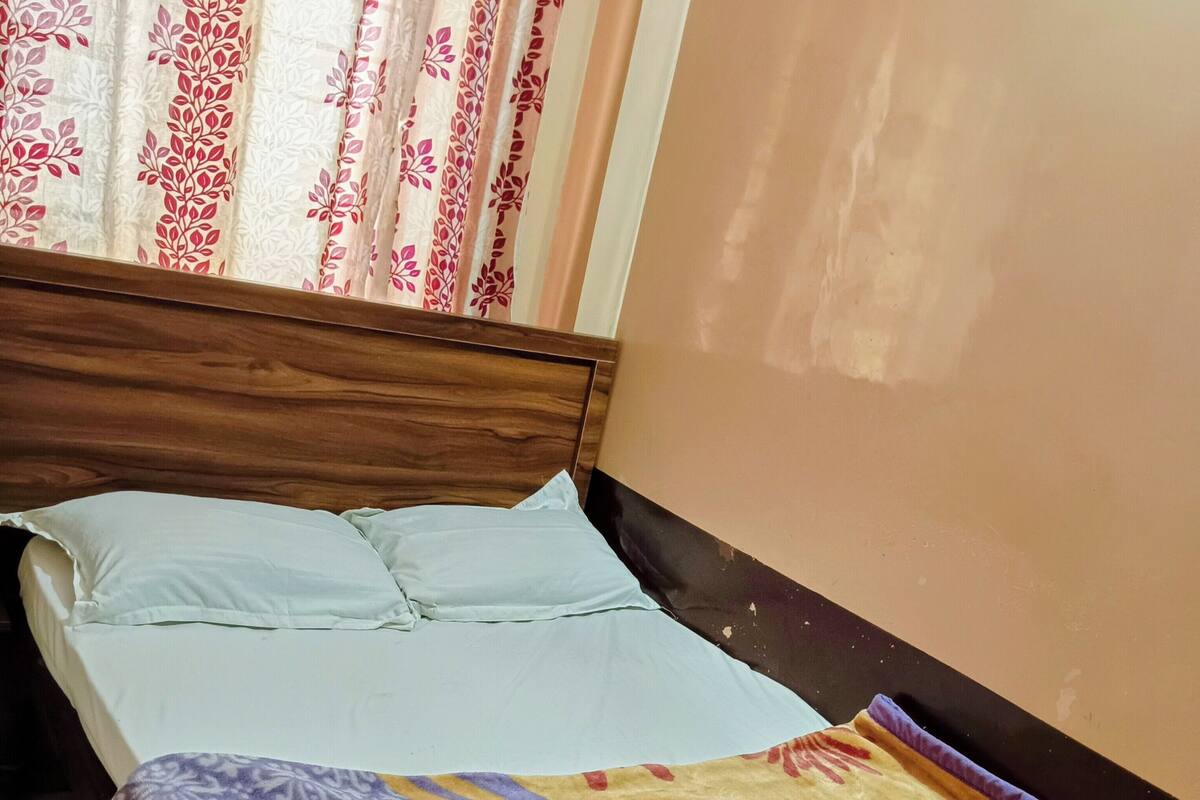 A bed with a patterned blanket, a wooden headboard, and a window with floral curtains.