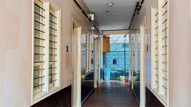 A long, narrow hallway with a tiled floor, flanked by walls with large windows and doors.