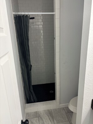 A bathroom with a shower, white tiled walls, a white toilet, and a door. - Peaceful Home in the Country (Hondo)