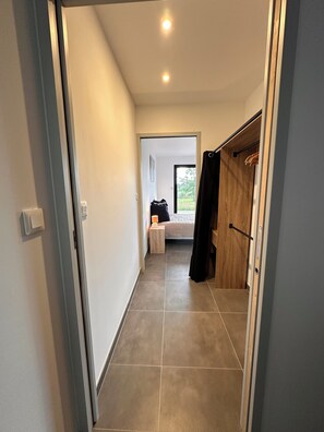 Ein Flur, der zu einem Schlafzimmer mit Bett, Nachttisch und Kleiderschrank führt.