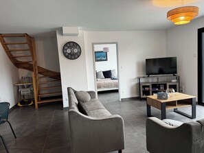 Ein modernes Wohnzimmer mit einer Couch, einem Fernseher, einem Holztisch und einer Treppe.