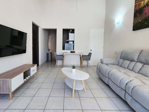 Ein modernes Wohnzimmer mit Flachbildfernseher, einer Couch, einem Esstisch mit Stühlen und einer Küchenzeile.