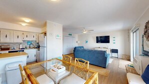 A modern kitchen with white cabinets, a dining area with a glass table, and a living room with a blue sofa. - Lee Ko 19 (Ocean City)