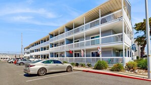 A multi-story motel with balconies, a parking lot, and a clear sky. - Lee Ko 19 (Ocean City)
