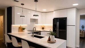 Een moderne keuken met een centraal eiland, roestvrijstalen apparatuur en hanglampen.