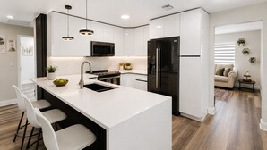 Een moderne keuken met een centraal eiland, barkrukken, een magnetron en een koelkast.
