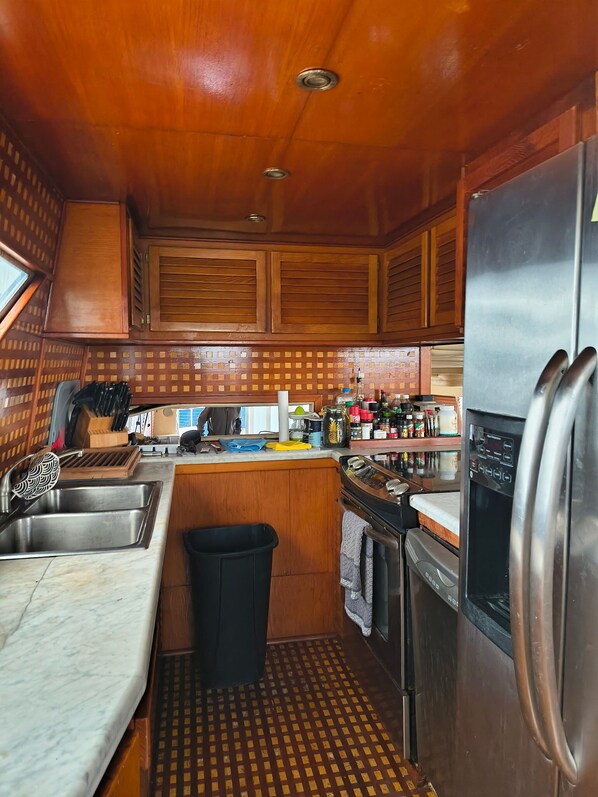Une cuisine compacte avec des meubles en bois, un évier en acier inoxydable, un réfrigérateur et une petite poubelle.