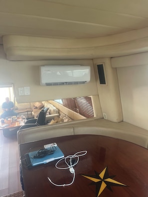 A room with a wooden table, a laptop, and a star decoration. There is a window with blinds, a beige sofa, and an air conditioning unit mounted on the wall.
