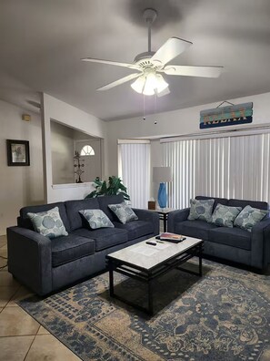 Ein Wohnzimmer mit zwei Sofas, einem Couchtisch, einem Deckenventilator und einem Schild mit der Aufschrift 'RELAX'.