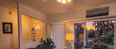 A living room with two sofas, a coffee table, a ceiling fan, a window with curtains, and a view of the outdoors.