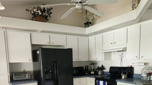 Una cucina con mobili bianchi, un frigorifero nero, un forno a microonde, un fornello e una ventola a soffitto.