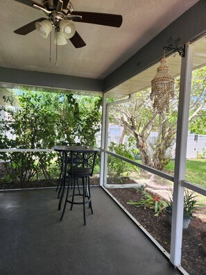 Eine überdachte Terrasse mit Deckenventilator, Tisch und Stühlen sowie einer Hängelampe.