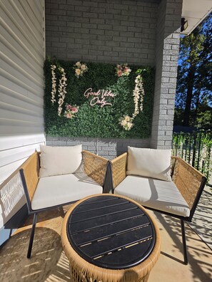 A corner seating area with a woven chair and a round table, a decorative wall with a floral arrangement, and a 'Good Vibes Only' sign. - Cozy home away from home (Matthews)