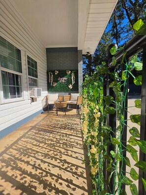 A covered outdoor seating area with a sofa and chairs, a wall with climbing plants, and a clear sky. - Cozy home away from home (Matthews)