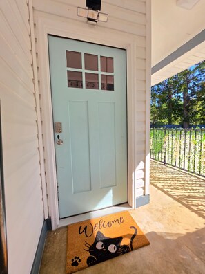 A light blue door with a window, a welcome mat with a cat design, and a covered porch area. - Cozy home away from home (Matthews)
