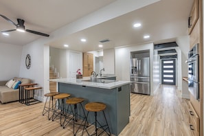A modern kitchen with a central island, bar stools, a ceiling fan, and built-in appliances.