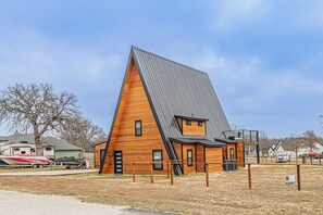 A wooden cabin with a sloped roof, a small attached structure, and a fenced yard.