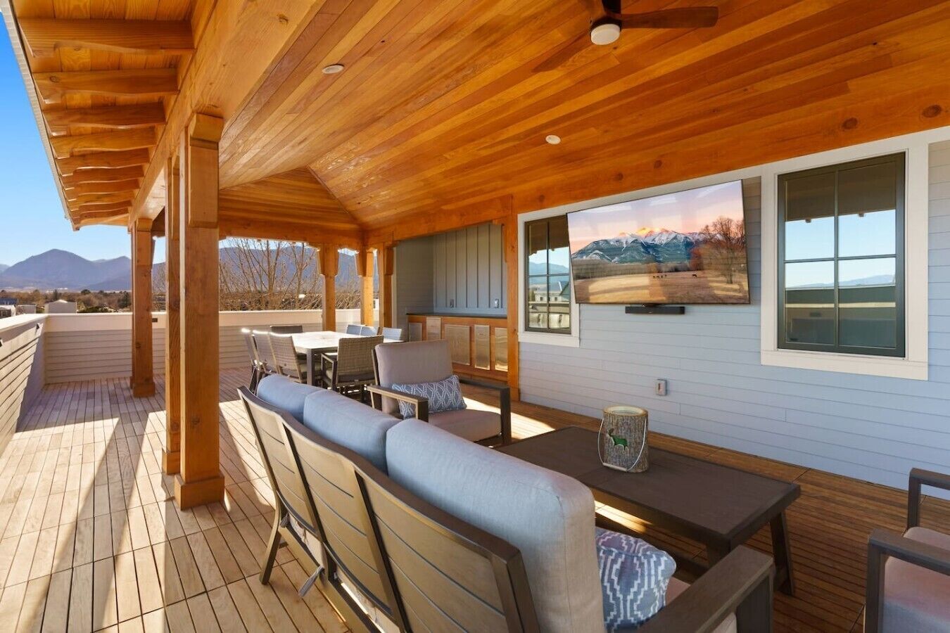 An outdoor patio with wooden furniture, a dining table, and a view of mountains.