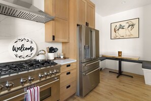 A modern kitchen with a gas stove, oven, stainless steel refrigerator, wooden cabinets, and a welcome sign. - Rooftop Views | House + Apt | Walk to Downtown (Buena Vista)