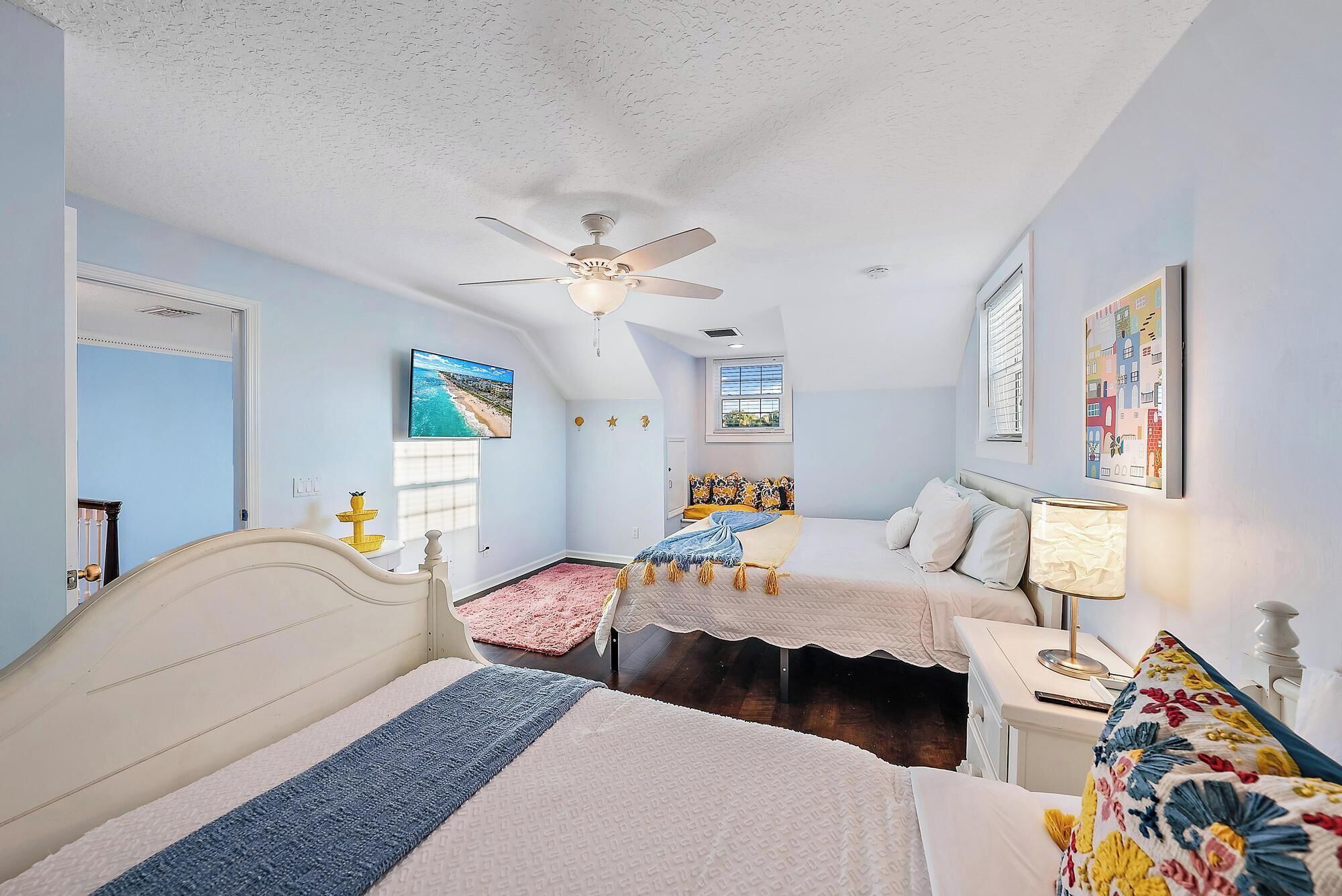 A bedroom with two beds, a ceiling fan, a TV, and artwork on the walls.