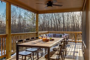 Eine überdachte Terrasse mit Holztisch, gedeckt für ein Frühstück, umgeben von Stühlen und einer Couch.