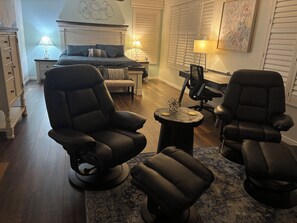 Ein modernes Wohnzimmer mit einem großen Bett, zwei schwarzen Ledersesseln, einem kleinen runden Tisch und einem Schreibtisch mit einem Computer.