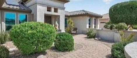 A residential property with a paved driveway, a small garden with shrubs, and a clear sky.