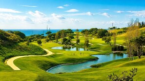Ein Golfplatz mit Teich, Bäumen und Blick auf den Ozean.