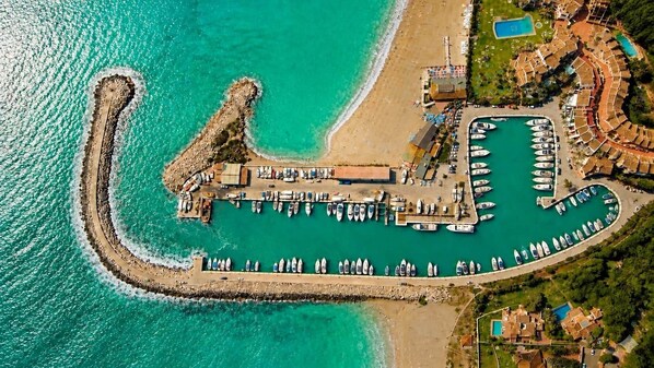 Luftaufnahme eines Küstenresorts mit Hafen, Strand und Poolbereich.