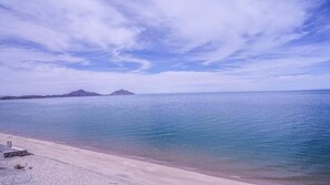Une plage à l’eau claire, avec un rivage sablonneux et des montagnes qui se dessinent à l’horizon.