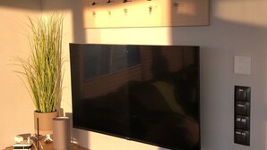 Ein Flachbildfernseher an der Wand, ein Blumentopf, ein Schreibtisch mit einem Laptop und ein an der Wand befestigtes Bedienfeld.