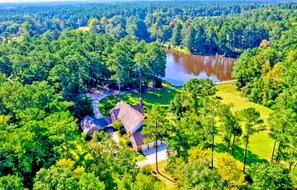 An aerial view of a property with a large lake, dense forest, and a house with a red roof.