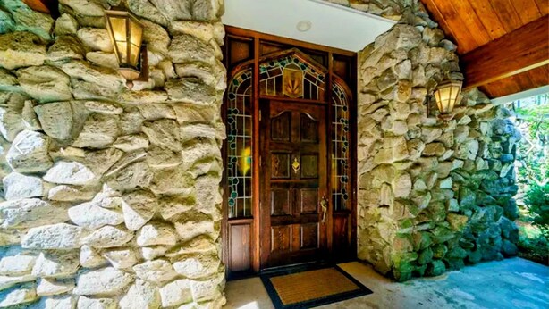 Une entrée en pierre avec une porte en bois, deux lanternes et un paillasson.