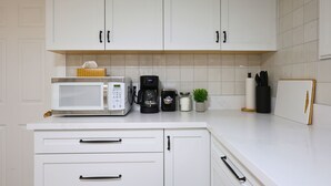 Uma cozinha com armários brancos, micro-ondas, cafeteira e uma pequena planta em vaso.