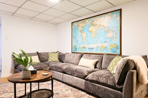 Un soggiorno con una grande mappa del mondo, un divano grigio, un tavolino con una pianta e un tappeto decorato.