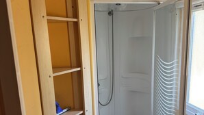 A compact bathroom with a shower enclosure, a built-in shelf unit, and a window.
