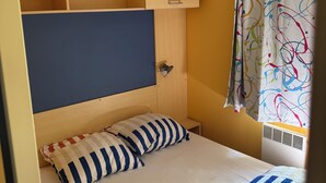 A compact room with a bed, a small bedside table, a headboard, a ceiling light, and a window with a curtain.