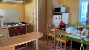 A compact kitchen with a gas stove, microwave, and cabinets. There is a dining table with chairs, and a window with curtains.